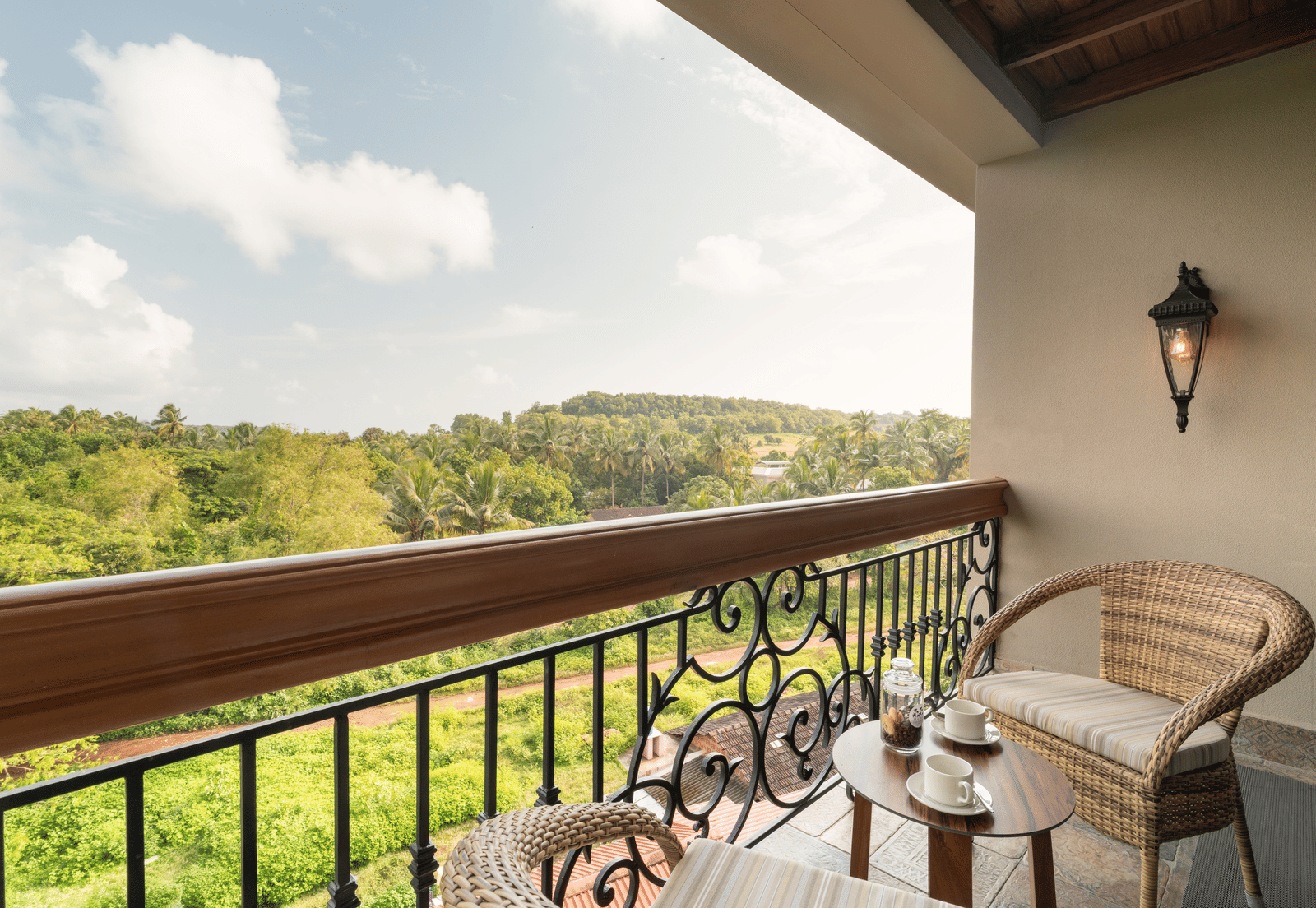 An expansive balcony with 2 arm chairs and a coffee table overlooking at the lush green lawn from the Classic Room (Diwa) at The Evren, Vagator.