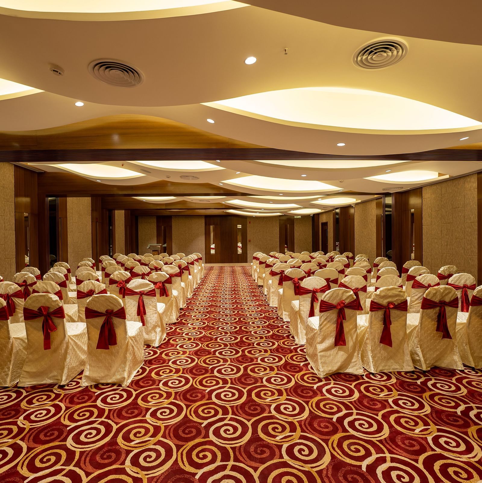 An image of a banquet hall set for an event with chairs draped in white covers and a red-and-white patterned carpet - The President Hotel, Kumara Park, Bangalore