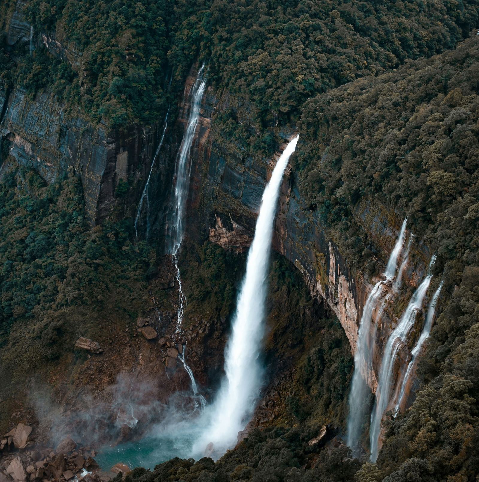Aerial view of the Seven Sisters Falls, where water cascades from towering cliffs draped in lush green trees.