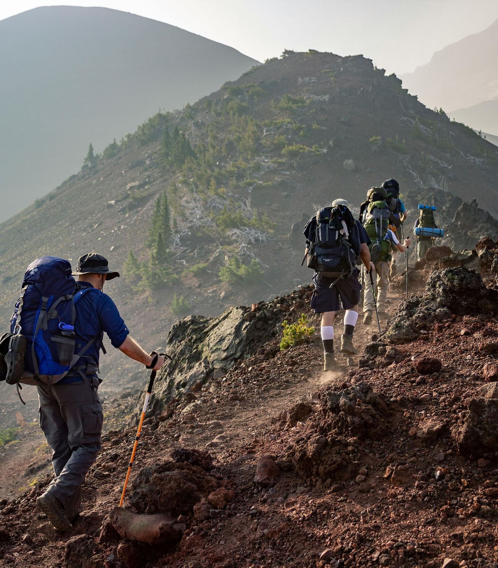 A group of hikers trekking along a rocky mountain trail with backpacks and trekking poles.