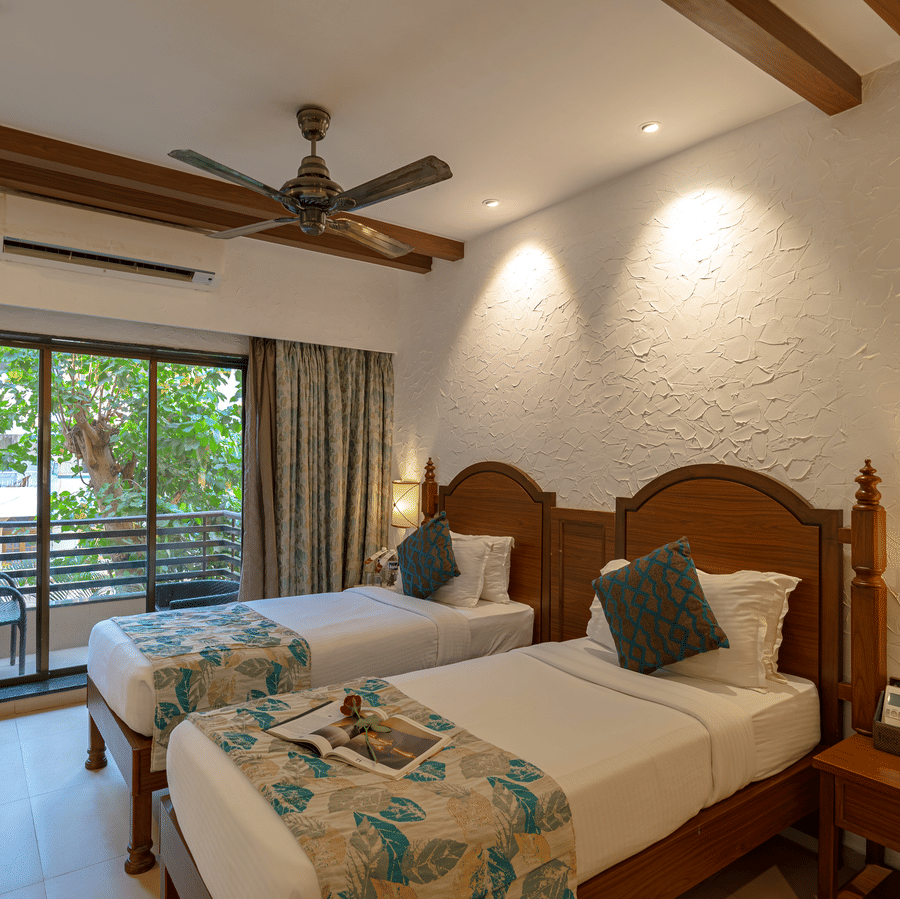 An image of a hotel room with twin beds dressed in white sheets, a cosy throw, wall-mounted lamps on each side, and an attached balcony.