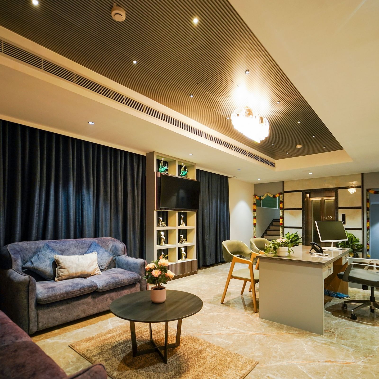 A  room includes a long table with chairs, a mounted television within shelving, window coverings, and ceiling lights - Hotel Park Inn, Nellore.