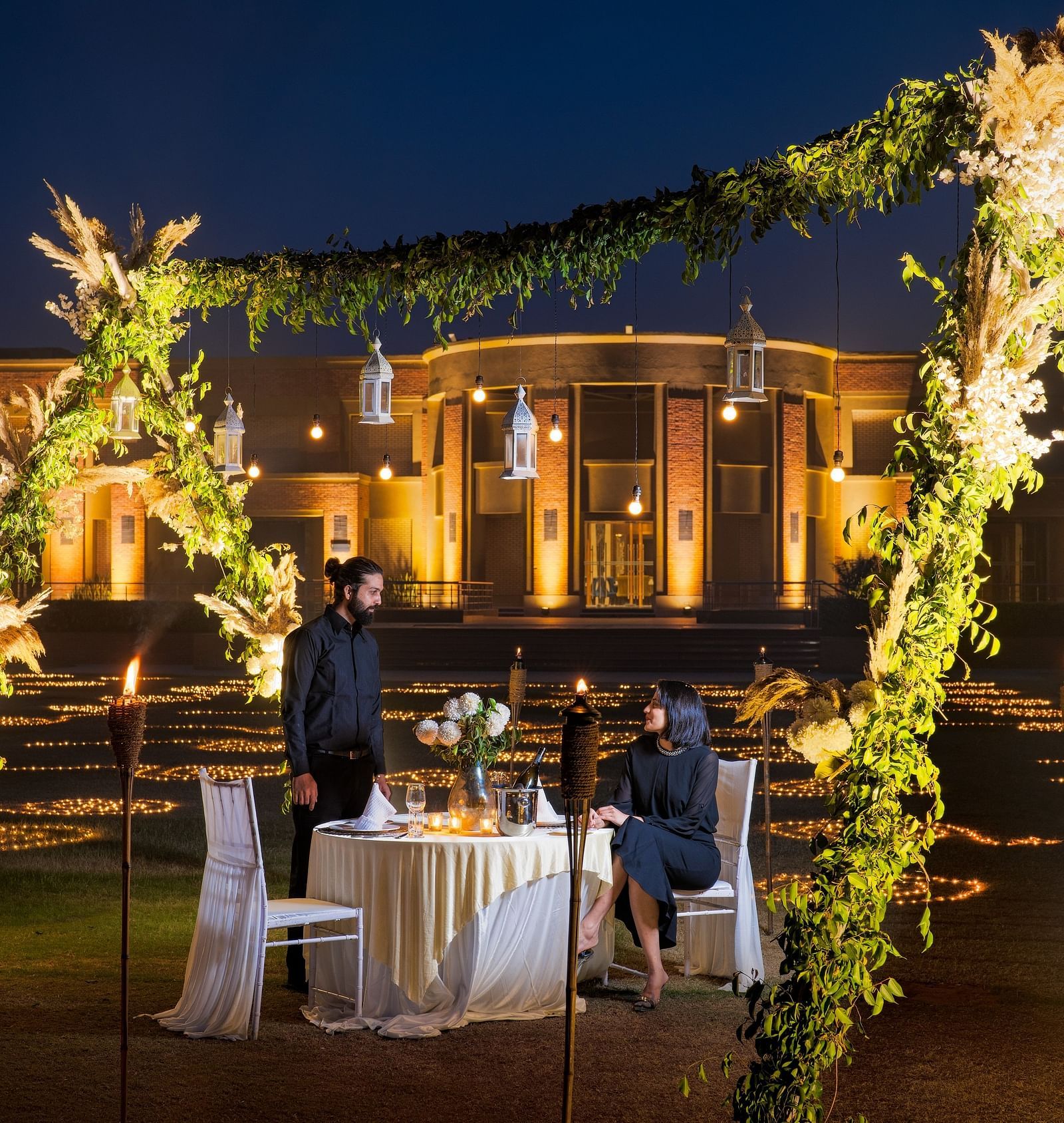 A couple enjoying dinner in an open-air setting surrounded by lavish decoration at Nirvana Luxury Hotel, Ludhiana.