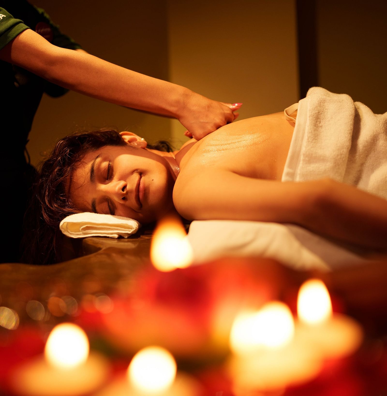 A person is receiving a massage with lit candles in the foreground, indicating a tranquil spa treatment area at Summit Enigma Resort and Spa