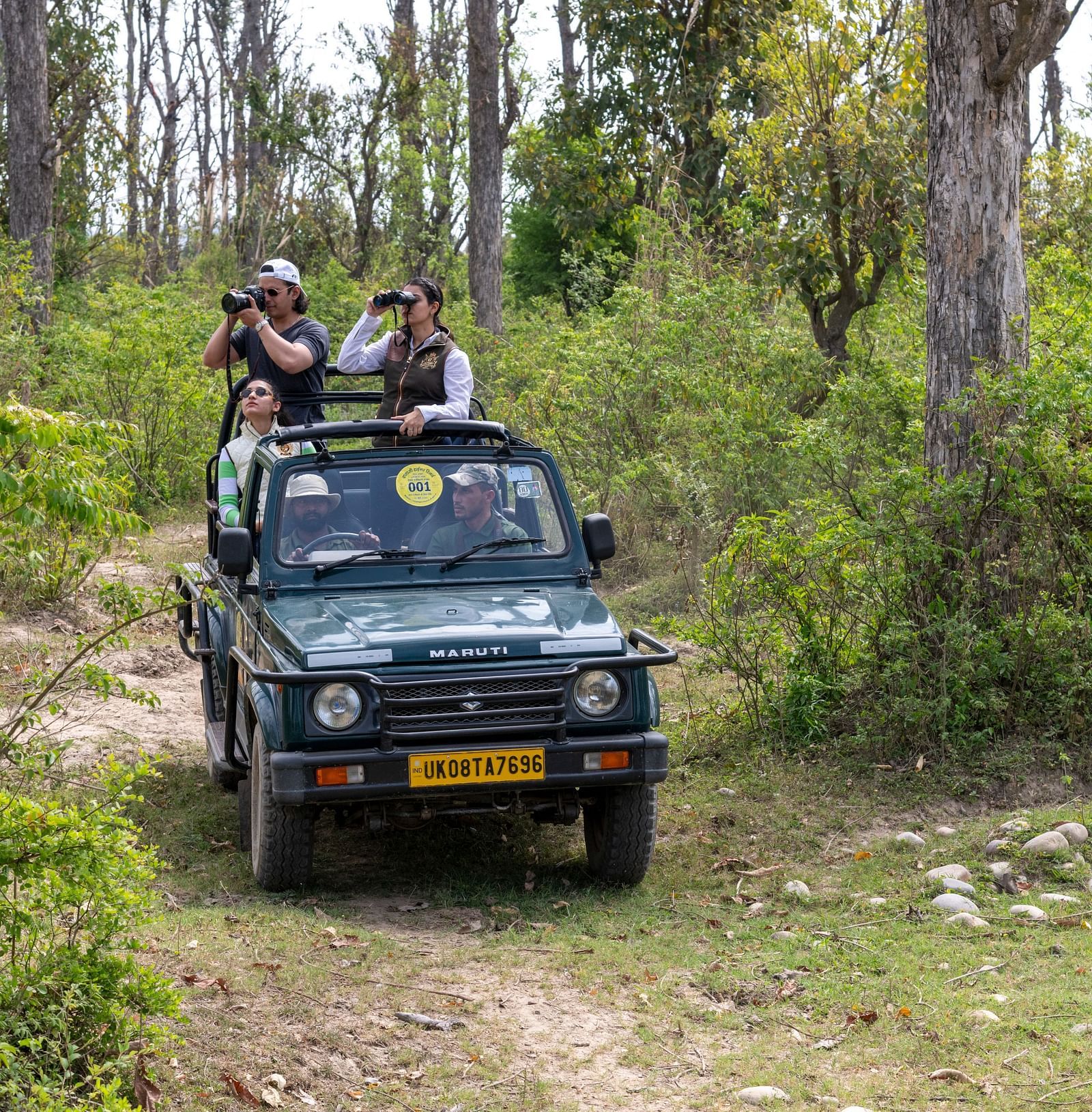 A car driving through dry grass lands during a safari at Rajaji National Park while people are looking at the fauna with binoculars - Aalia Jungle Resort & Spa