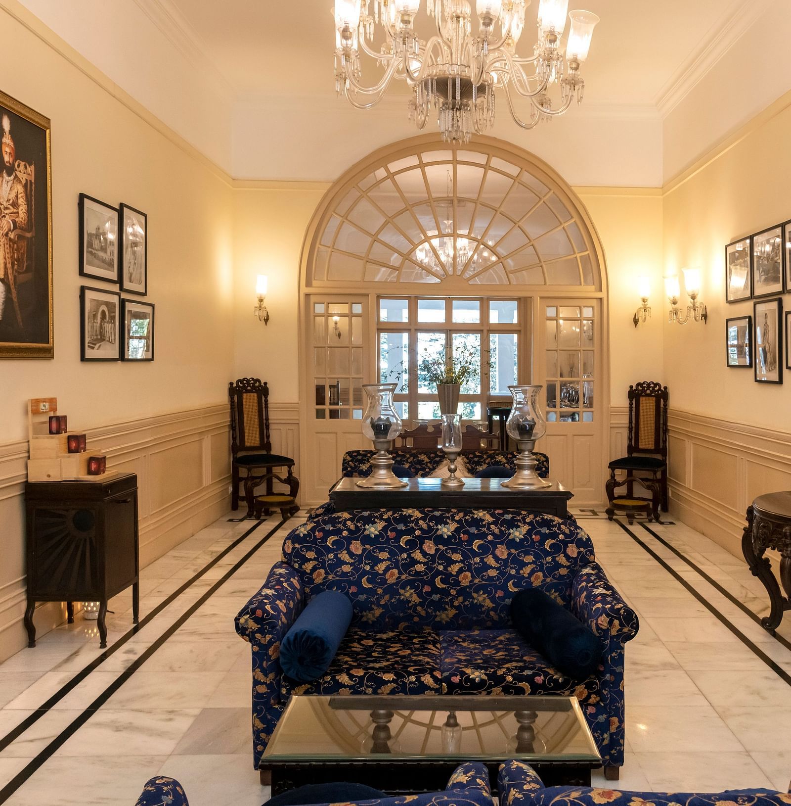 The lobby of The Claridges Nabha Residence in Mussoorie, featuring sofas, wall paintings, a chandelier, a mirror, and various decorative items.