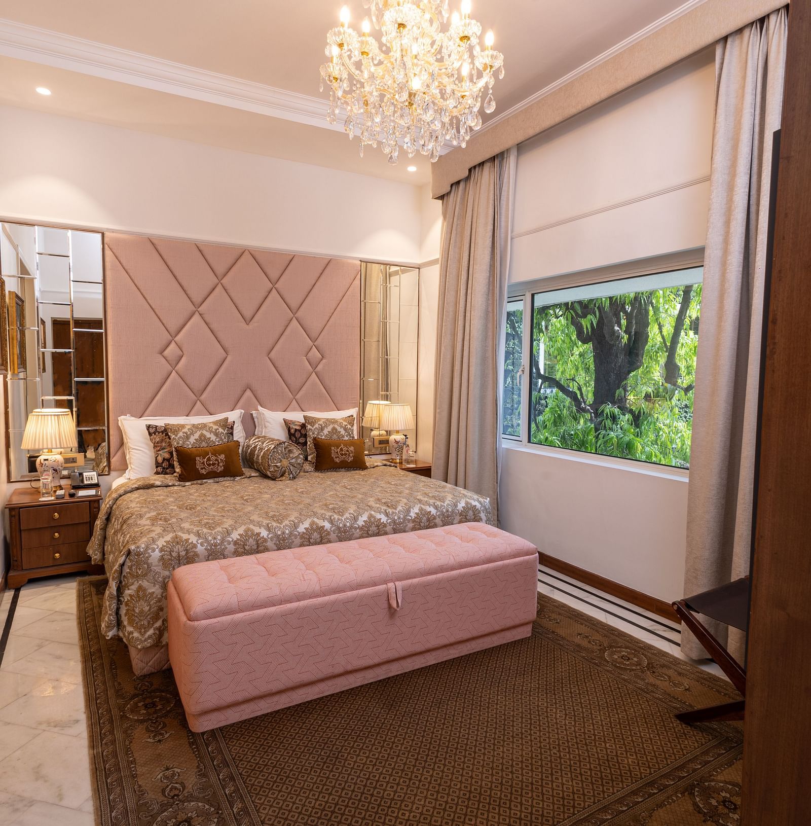 Luxury Suite at The Claridges New Delhi, featuring a cosy king sized bed with pillows and an elegant chandelier hanging overhead