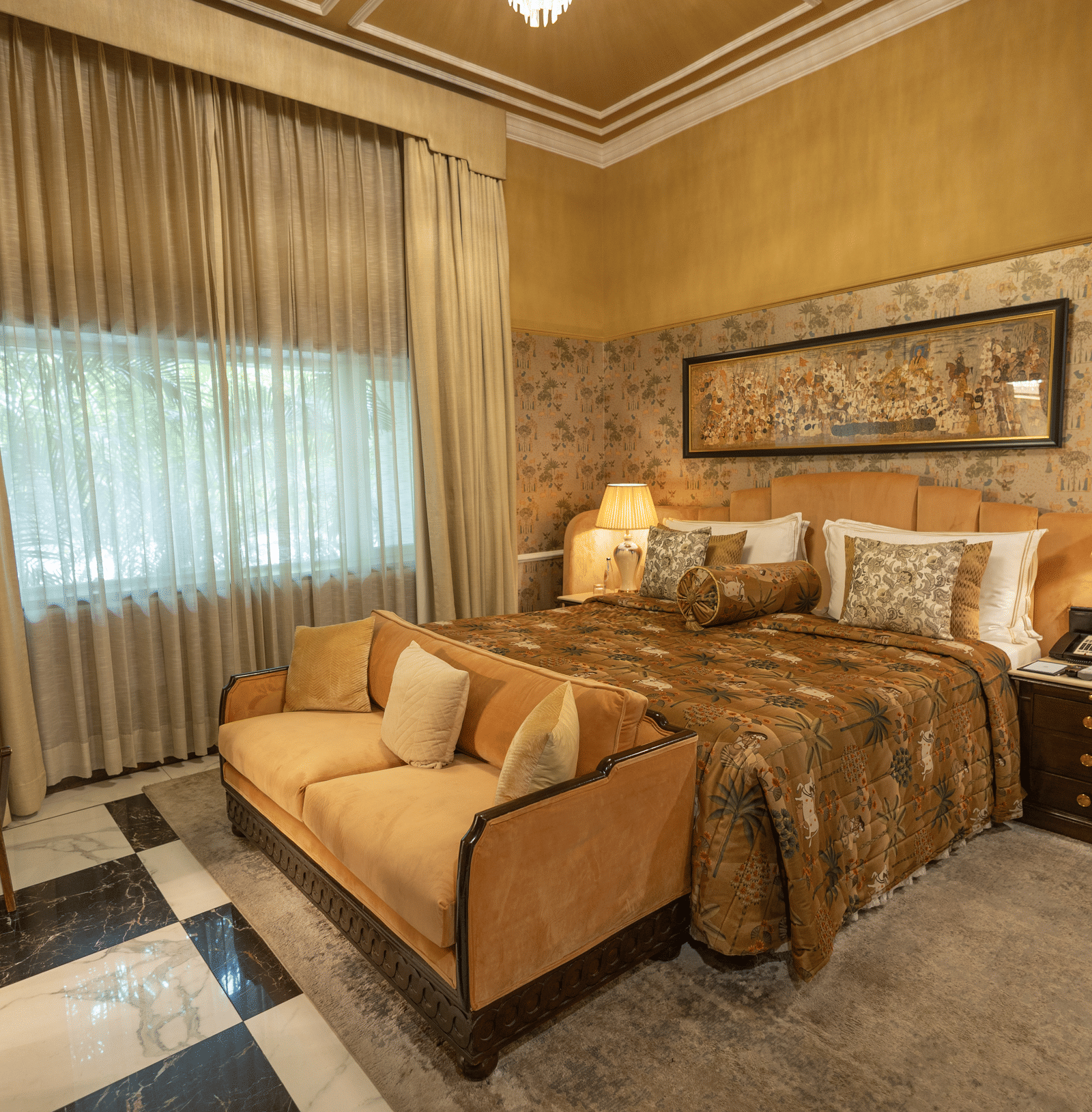 Executive Suite at The Claridges New Delhi, featuring a cosy king sized bed, a sofa placed in front, and a bedside lamp