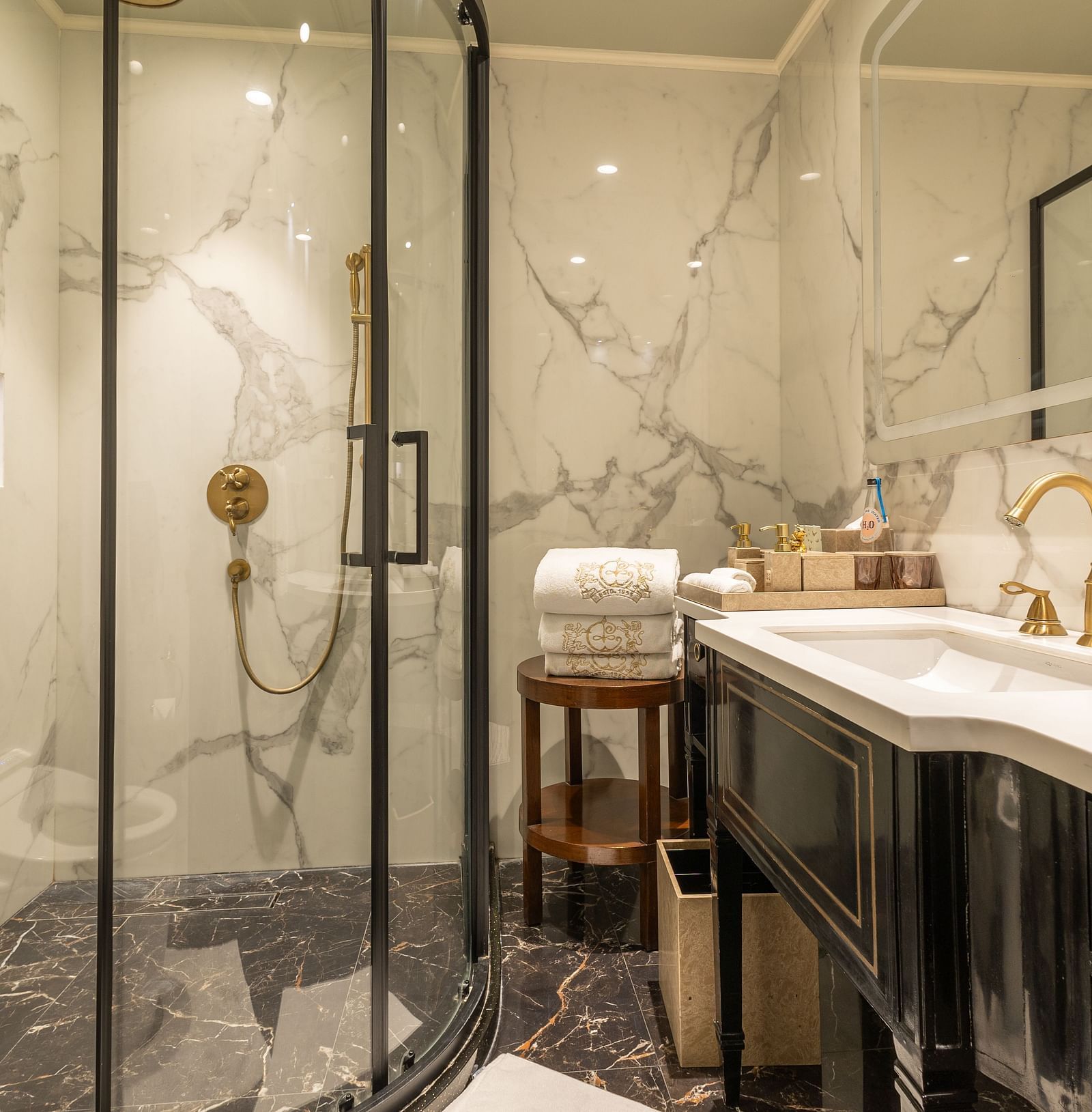 Luxury Suite with Whirlpool washroom at The Claridges New Delhi, featuring a sleek sink, wall-mounted mirror, and a glass-enclosed bath area