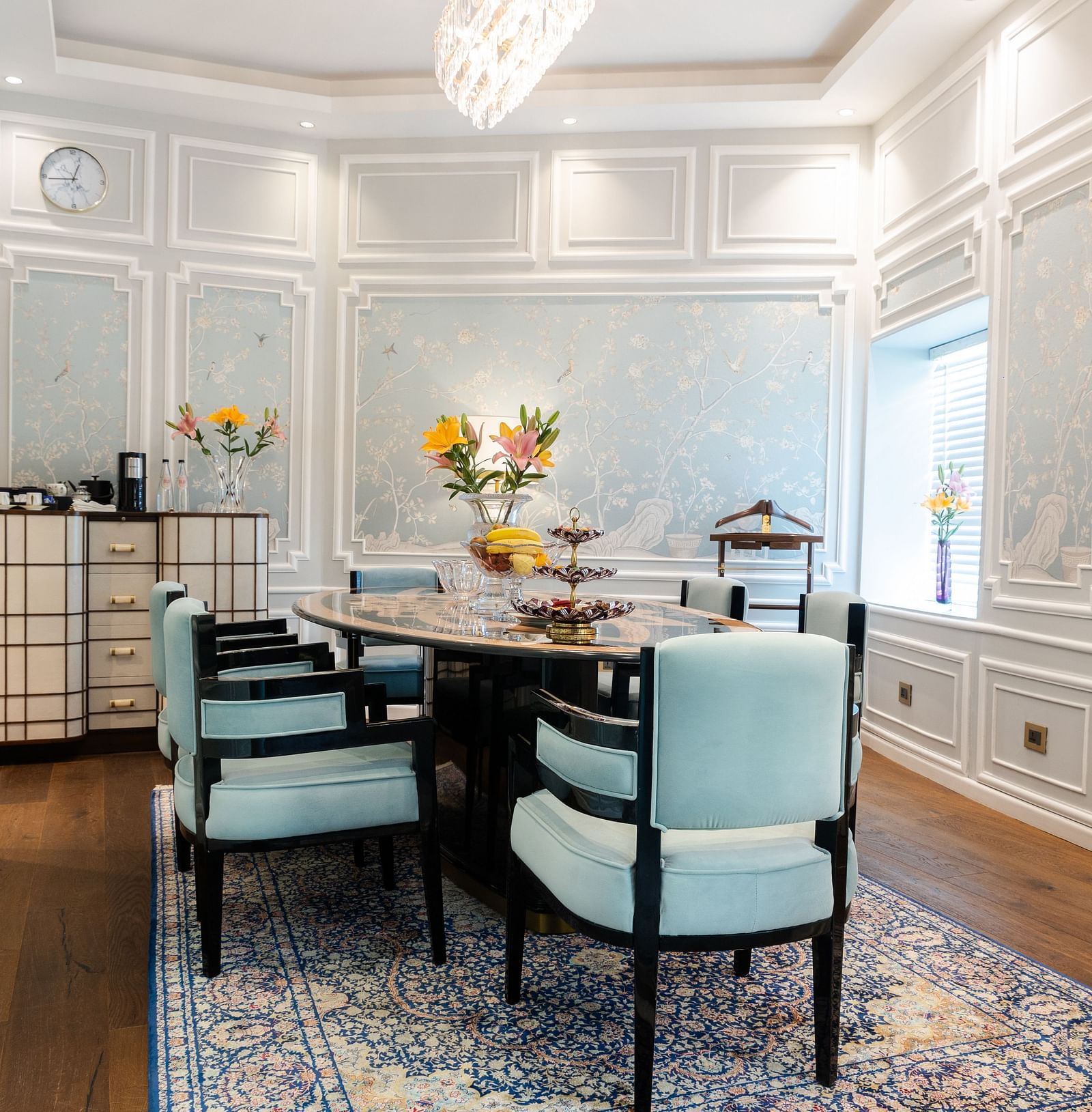 A dining table with blue cushioned chairs on either side in the living area of our Diplomatic suite in New Delhi at the Claridges