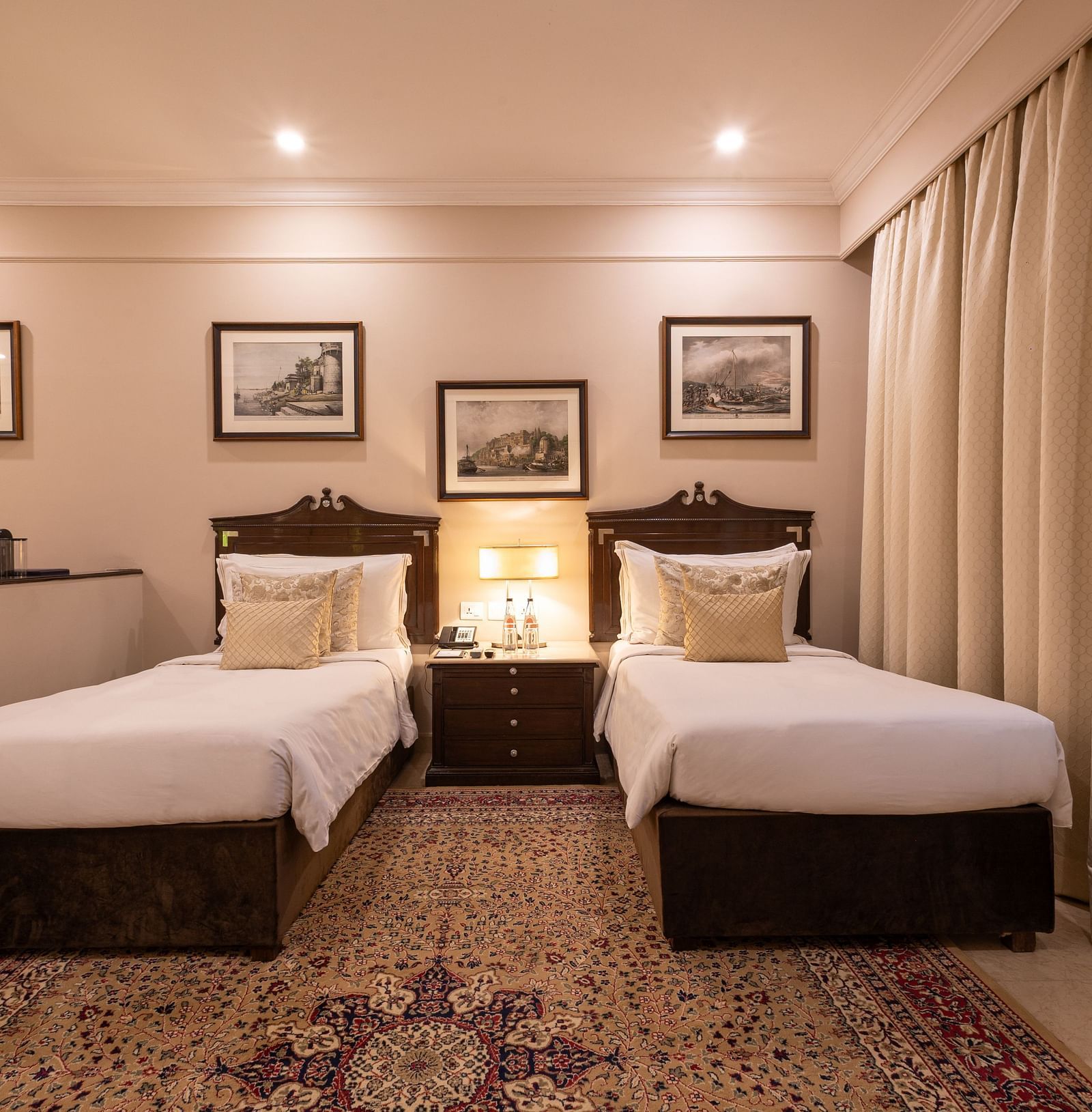 Front view of the Grand Luxury Twin Bed Room at The Claridges New Delhi, featuring elegant twin beds, a framed photo on the wall, and stylish ceiling lights