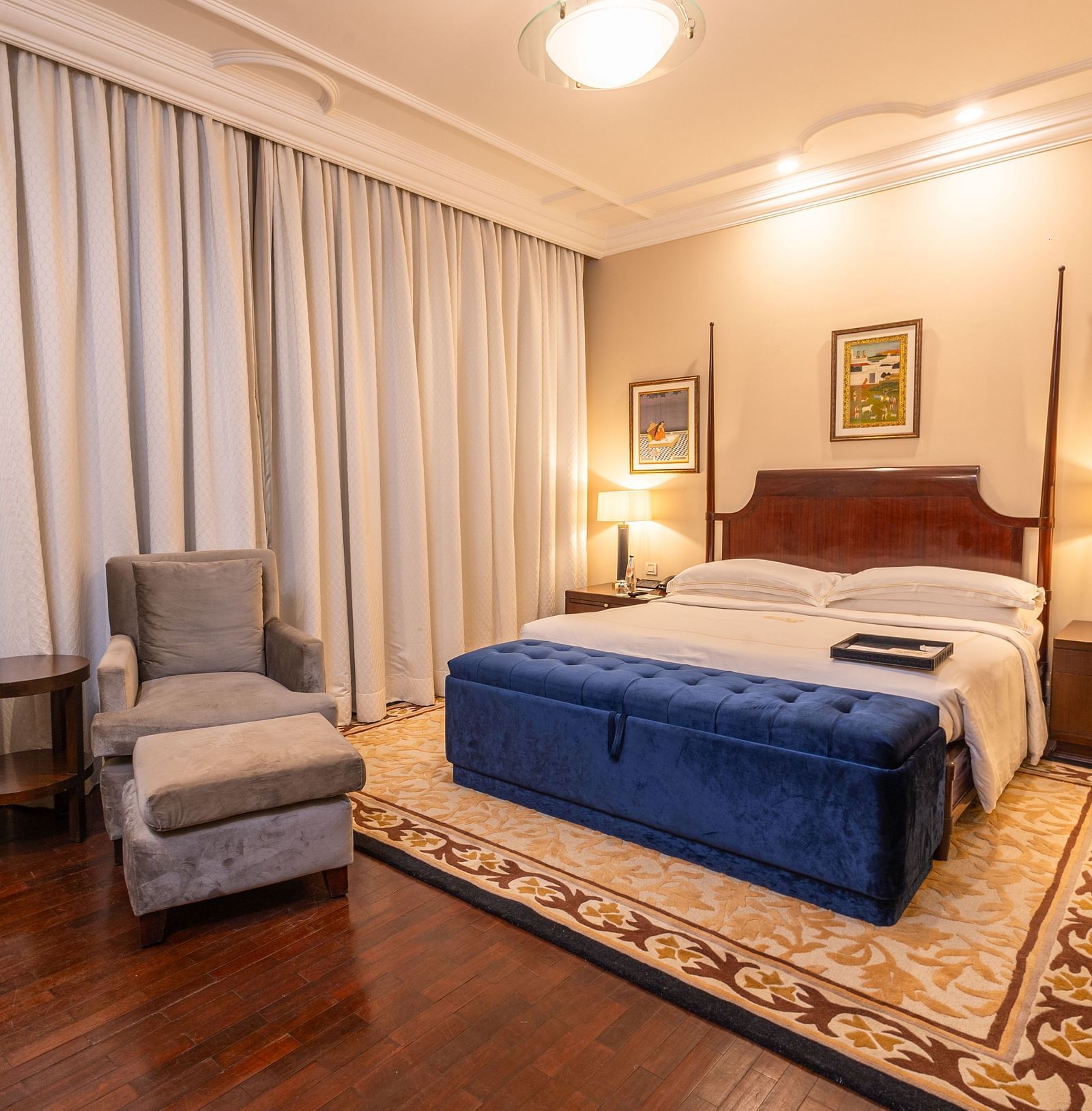 corner view of the luxurious bedroom at our heritage rooms with white curtains and a grey arm chair  - The Claridges New Delhi