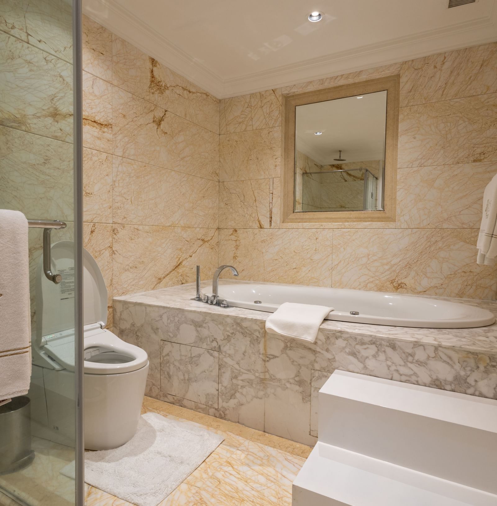 he Claridges New Delhi light-colored marble bathroom includes a toilet next to the large step-up bathtub.