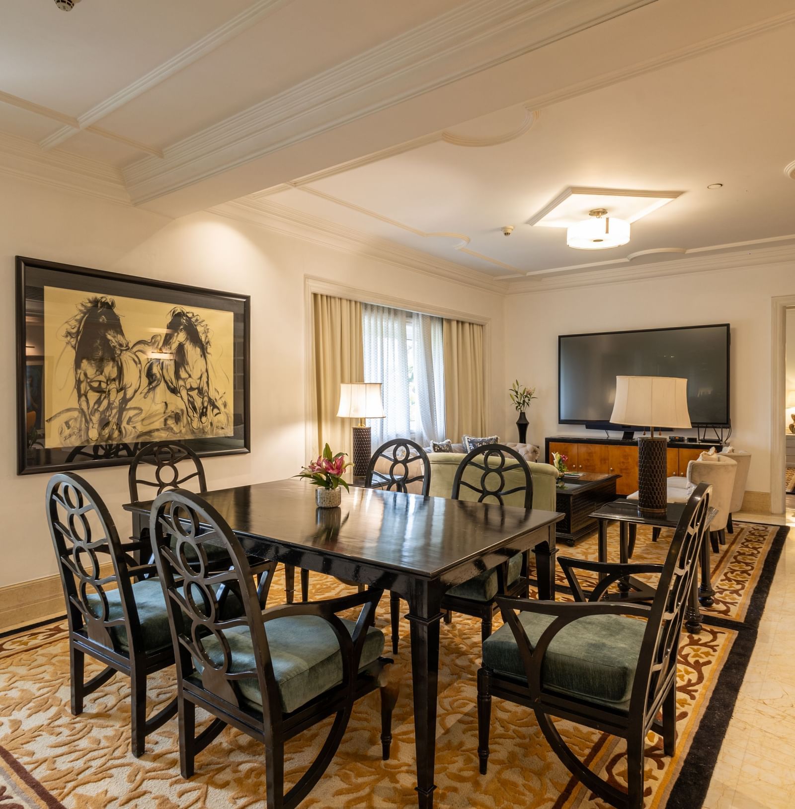 The Claridges New Delhi formal dining room is set with a dark table, black chairs, and a painting on the wall.