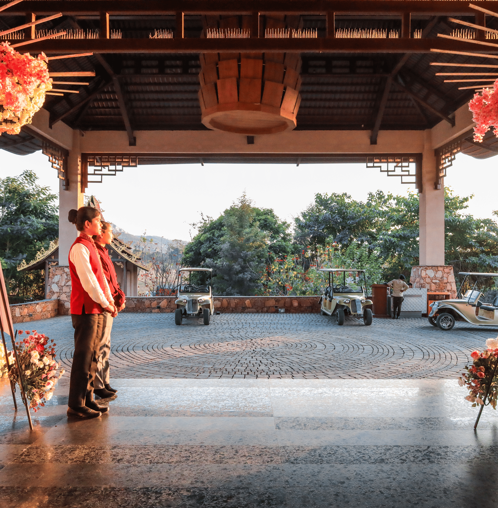 Staff members in red waistcoats stand near the entrance of Ananta Spa & Resort, Jaipur, framed by beautiful pink floral decorations.