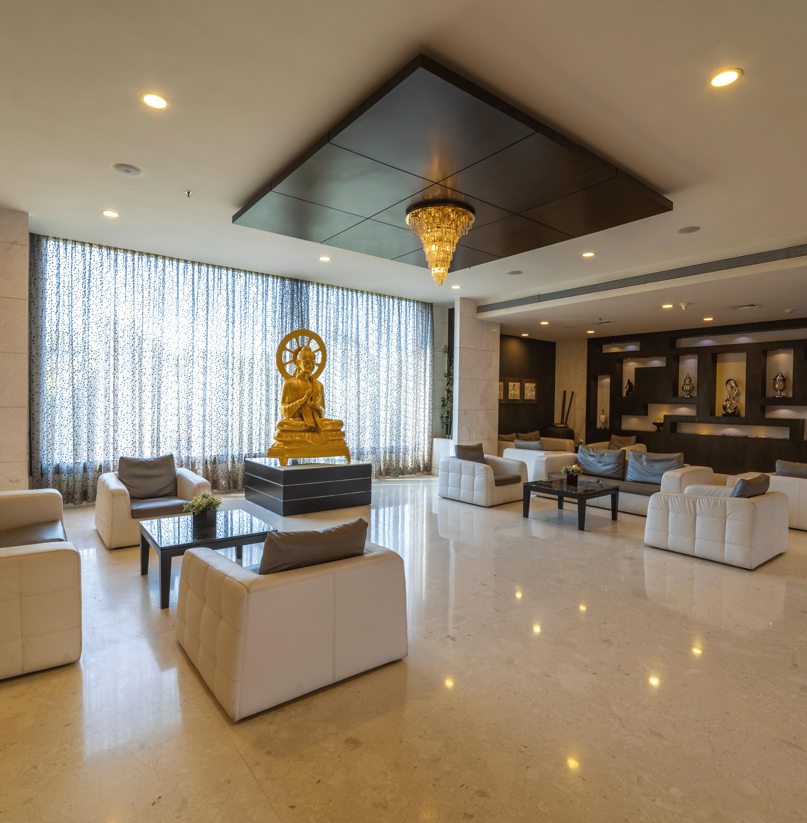 Hotel lobby area with amble seating and warm lighting, and a statue of an idol in the centre at Narayani Heights Hotel & Resorts, Ahmedabad.