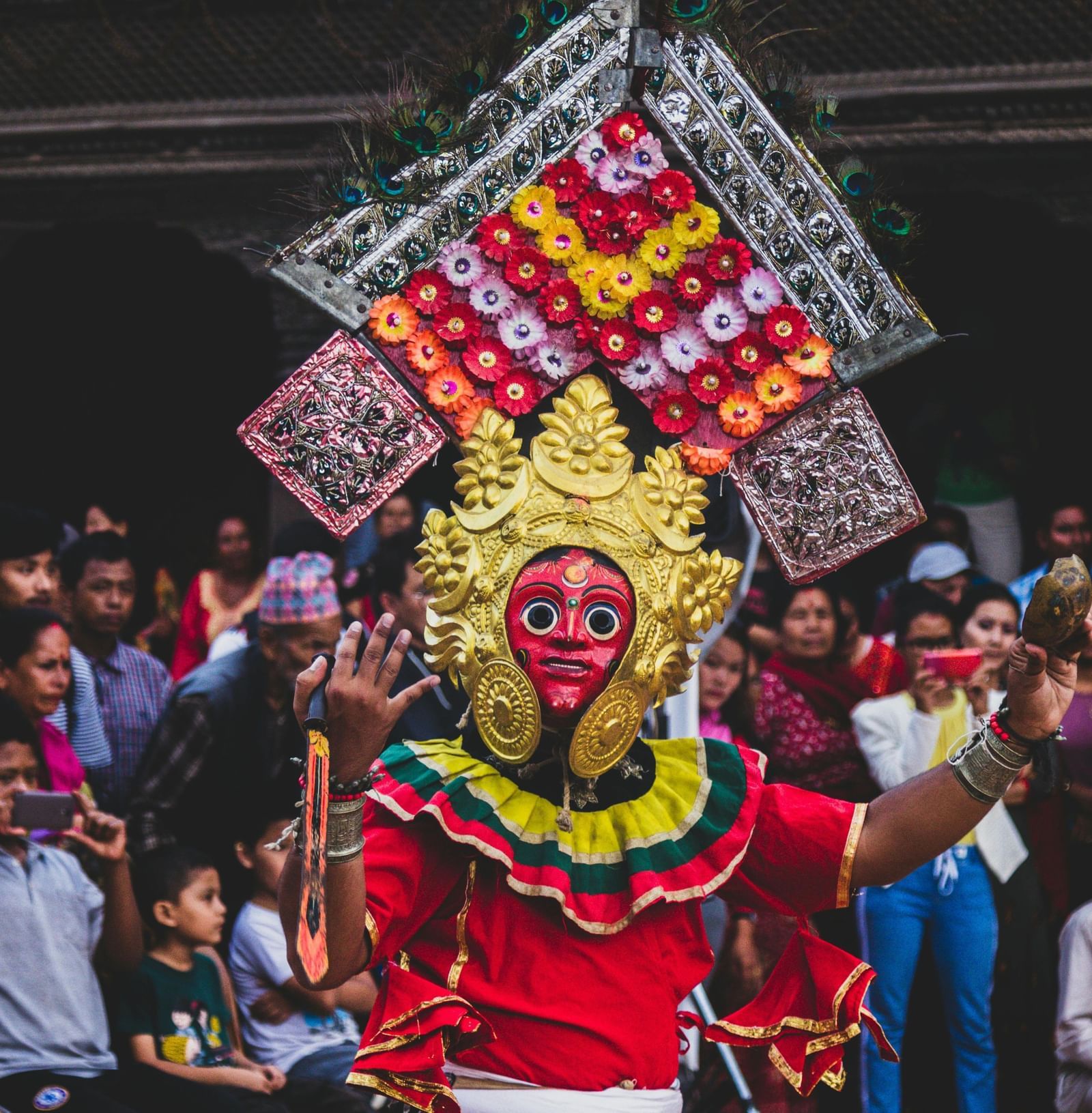 A person in a vibrant traditional costume and mask performing in front of a crowd.