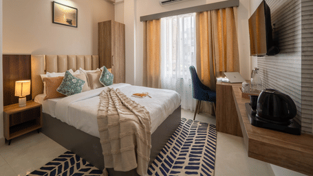A bedroom with king size bed, chair and desk, wall-mounted TV, and wardrobe at Perfectstayz Premium Kaashin, Varanasi.