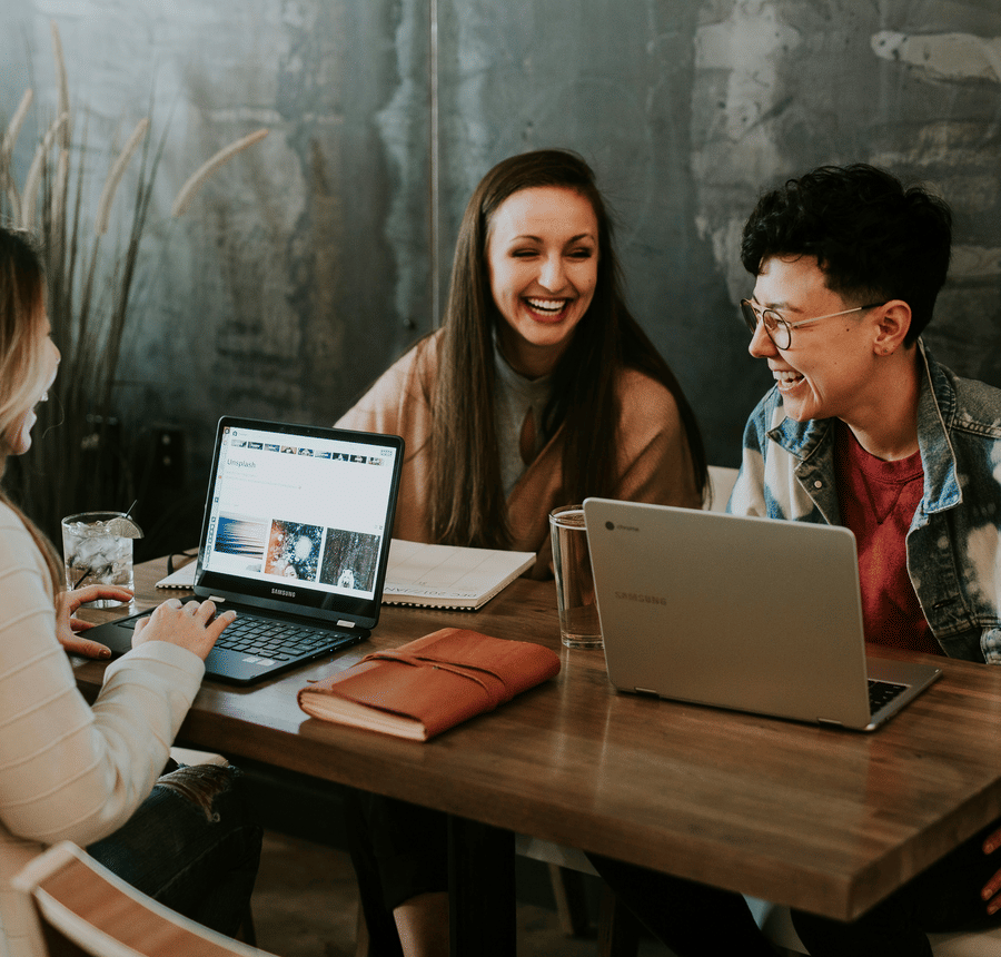 Three people sitting around a table laughing and working together on laptops at a cafe