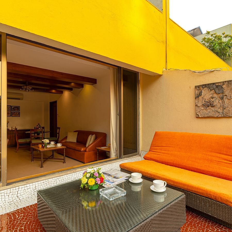 An image of a balcony attached to a room, showcasing an orange sofa and a small coffee table.
