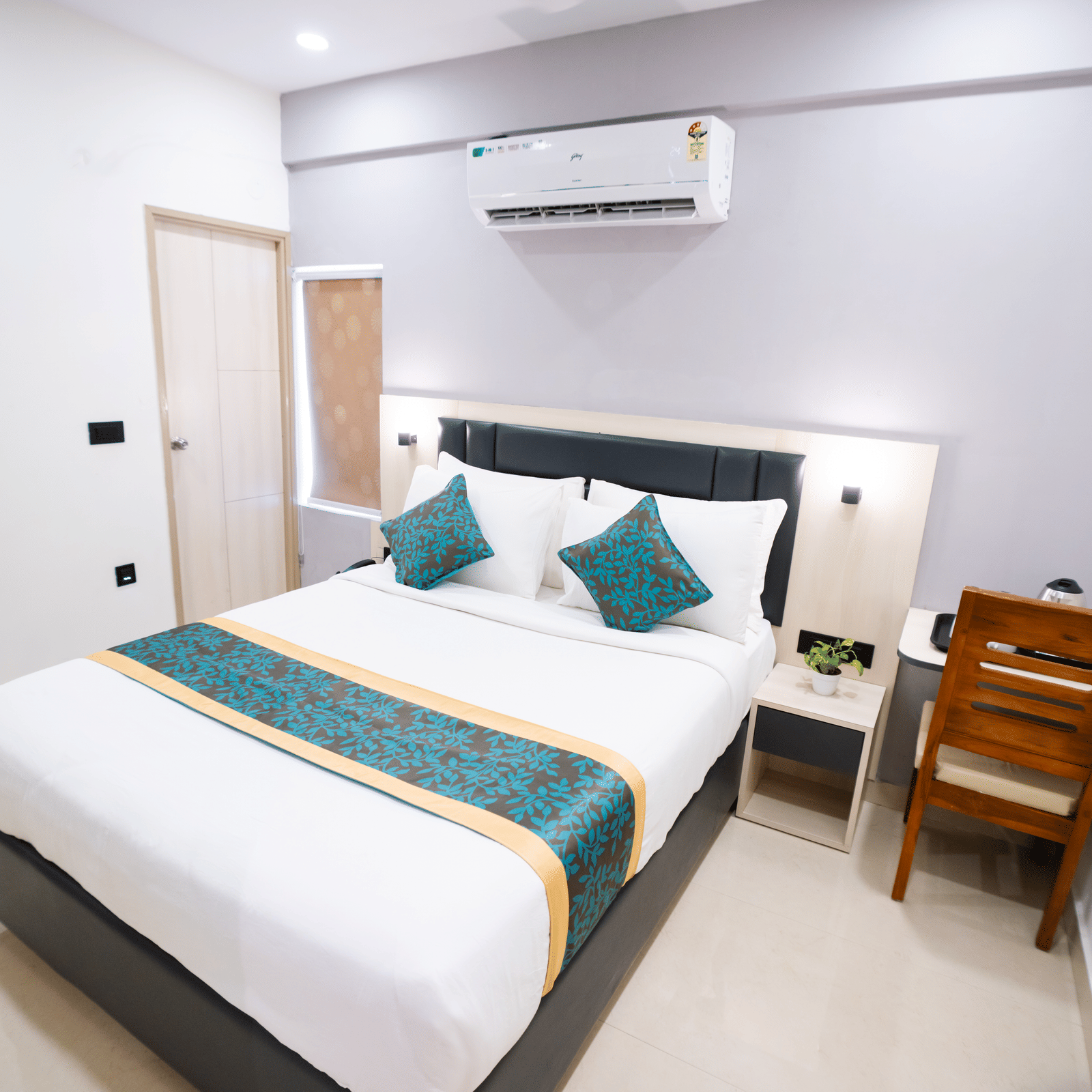 A room featuring a spacious bed, wall-mounted A/C above the headboard, a mirror, and a closed door to the side at Sunrise Business Hotel, Hyderabad.