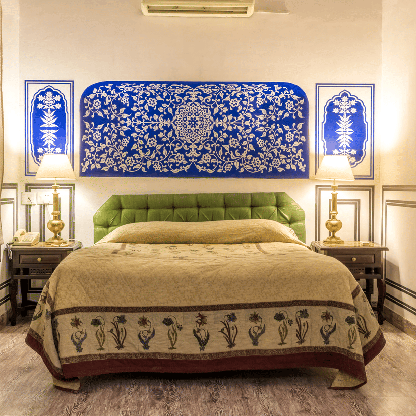 Deluxe Room at Mandawa Haveli, Jaipur featuring a king size bed, bedside table with lamps on either side, and a table with tea and coffee maker.