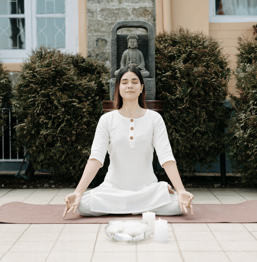 Woman practicing Pranayama yoga seated on the floor with green plants in the background