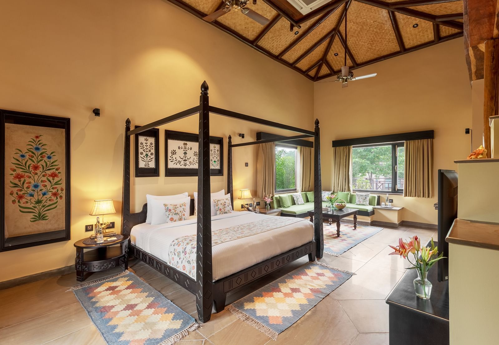 A luxurious bedroom with a dark wood four-poster bed and vibrant rug at Aamaghati Wildlife Resort.