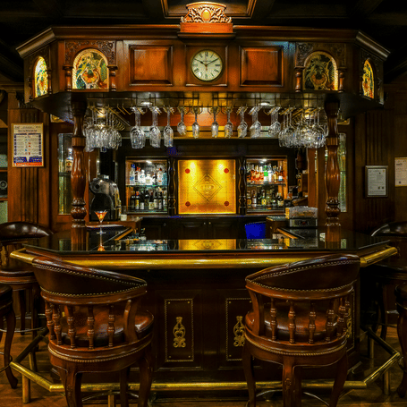 Baron and Baroness bar at MAYFAIR Lagoon, Bhubaneswar featuring a bar counter, liquor bottle in shelves behind the bar, and near the counter top there are chairs placed.