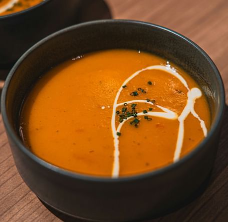 A bowl of creamy tomato soup garnished with herbs and a swirl of cream.