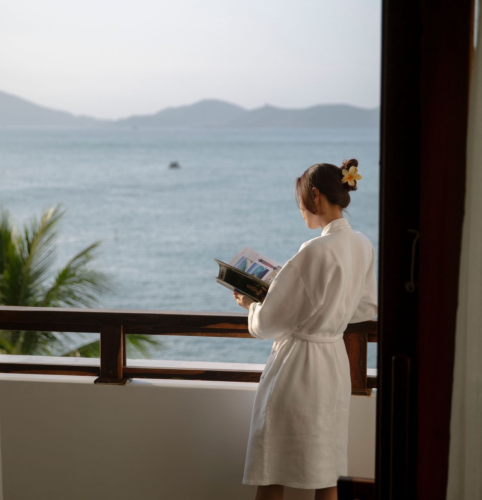 An image of a woman standing on the balcony An image of a huge sitting area of with several chairs and centre tables - Alibu Resort Nha Thrang