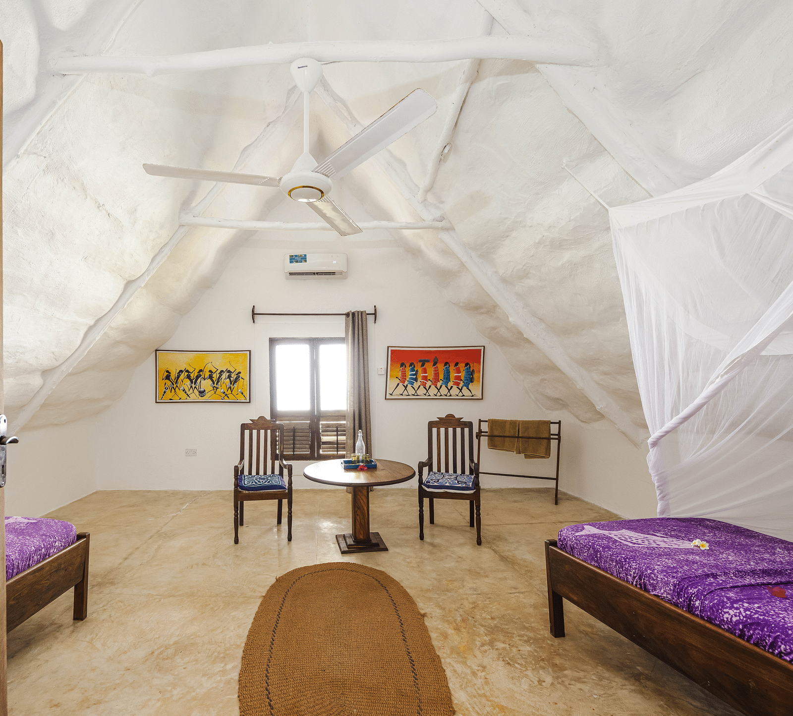 A cosy room with a wooden bed and a table with chairs with windows in the background offering natural light in Sea View Family Cottages - Shooting Star Boutique Hotel.