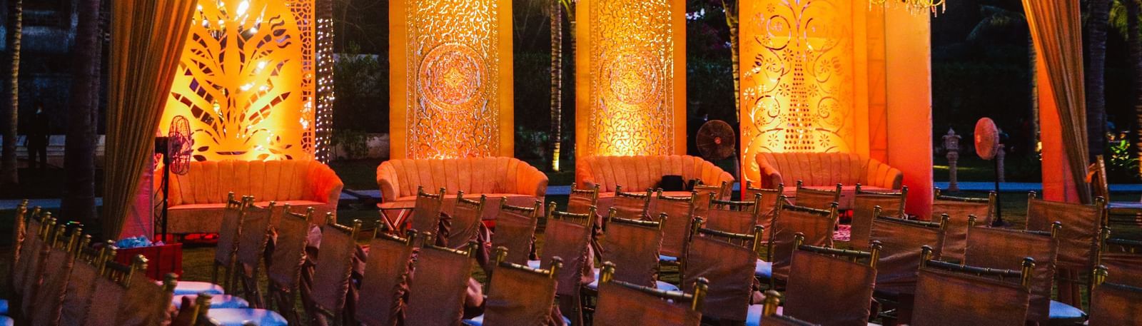 A stage draped with orange coloured cloth in the Sundarabagh lawn at Kaldan Samudhra Palace featuring chairs in theatre seating arrangement