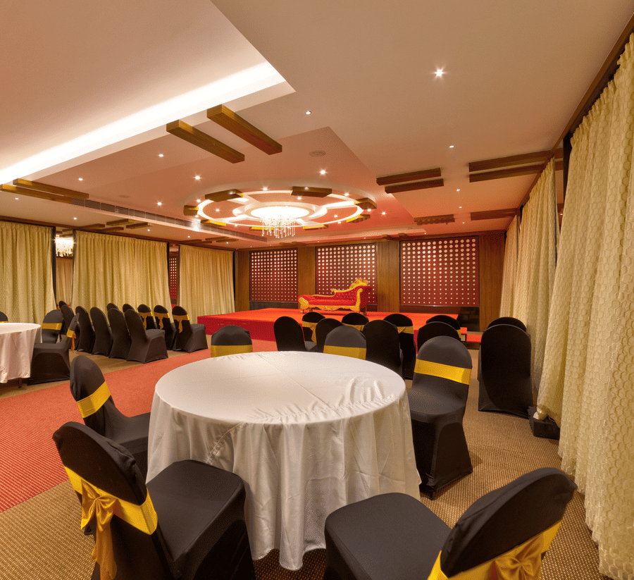 Round tables, black and gold chairs, a red carpet, and a stage setup inside the banquet hall of Icon Express By Bhagini, Mahadevapura.