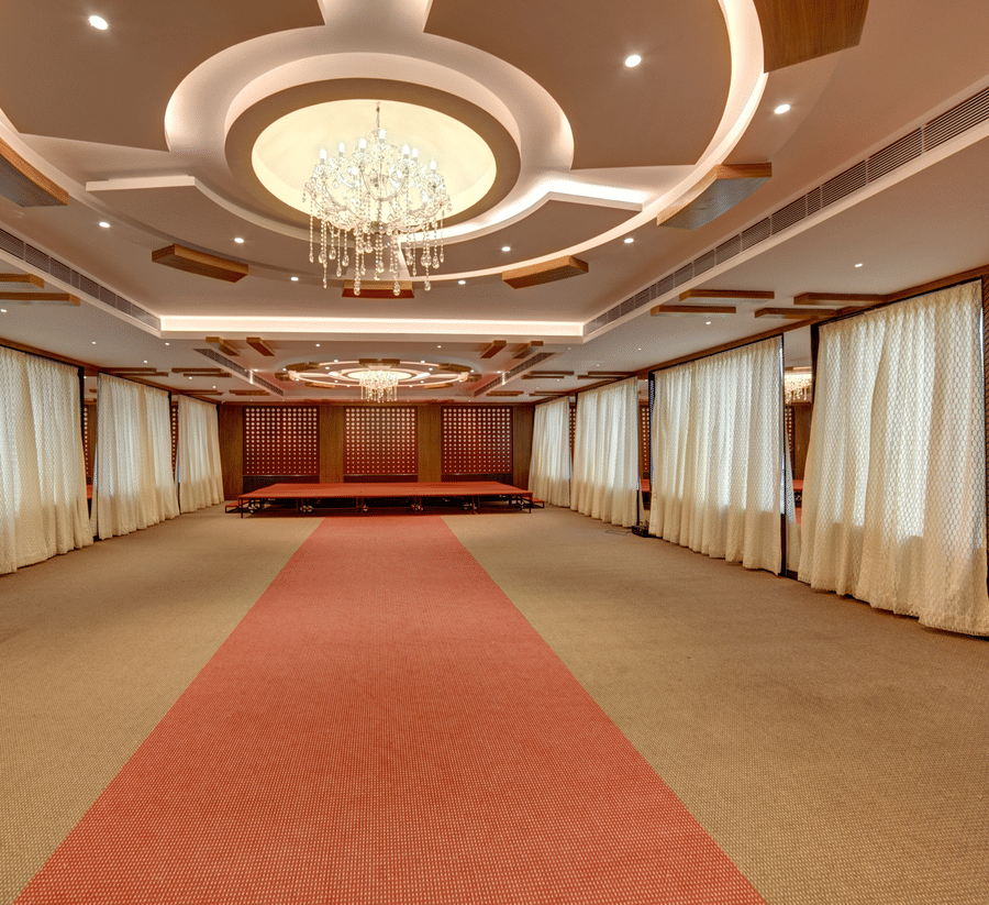 A spacious banquet hall with a red carpet in the centre, a decorative chandelier, and wooden walls at Icon Express By Bhagini, Mahadevapura.