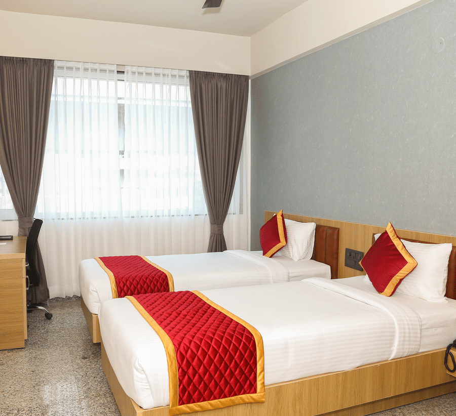 Two single beds, a window with curtains, and a wooden desk at Icon Express By Bhagini, Mahadevapura.