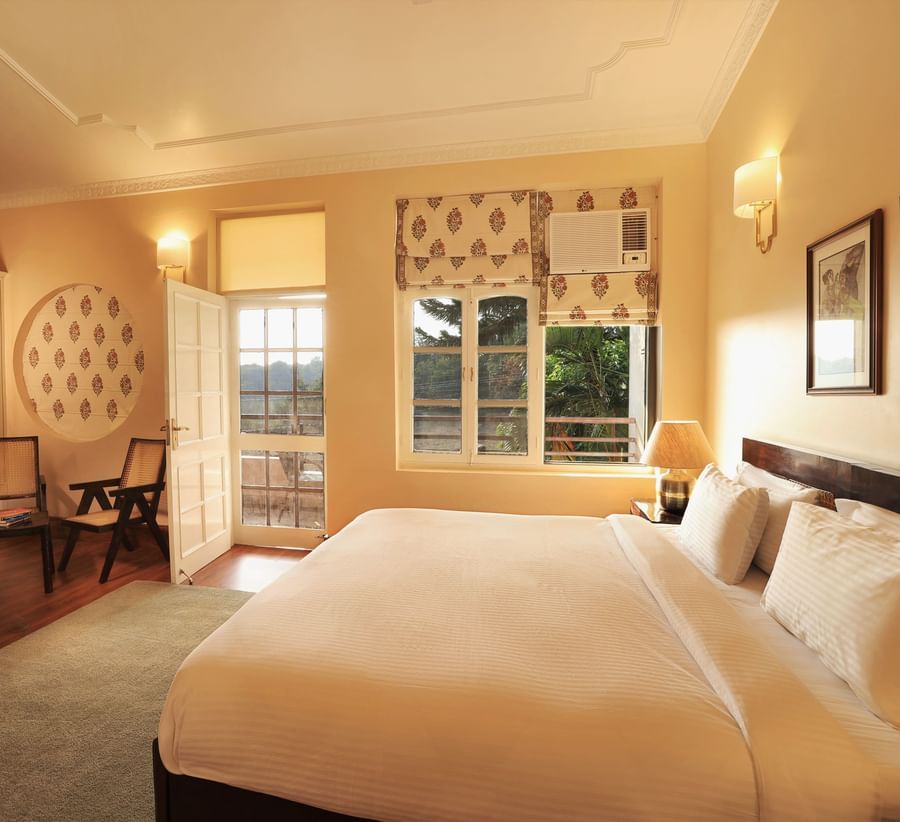 An image of a Super Deluxe Room featuring a double size bed, two chairs, a table where coffee maker is kept, and an open door from where sunlight is flooding the room - Lamrin Boutique Cottages Rishikesh
