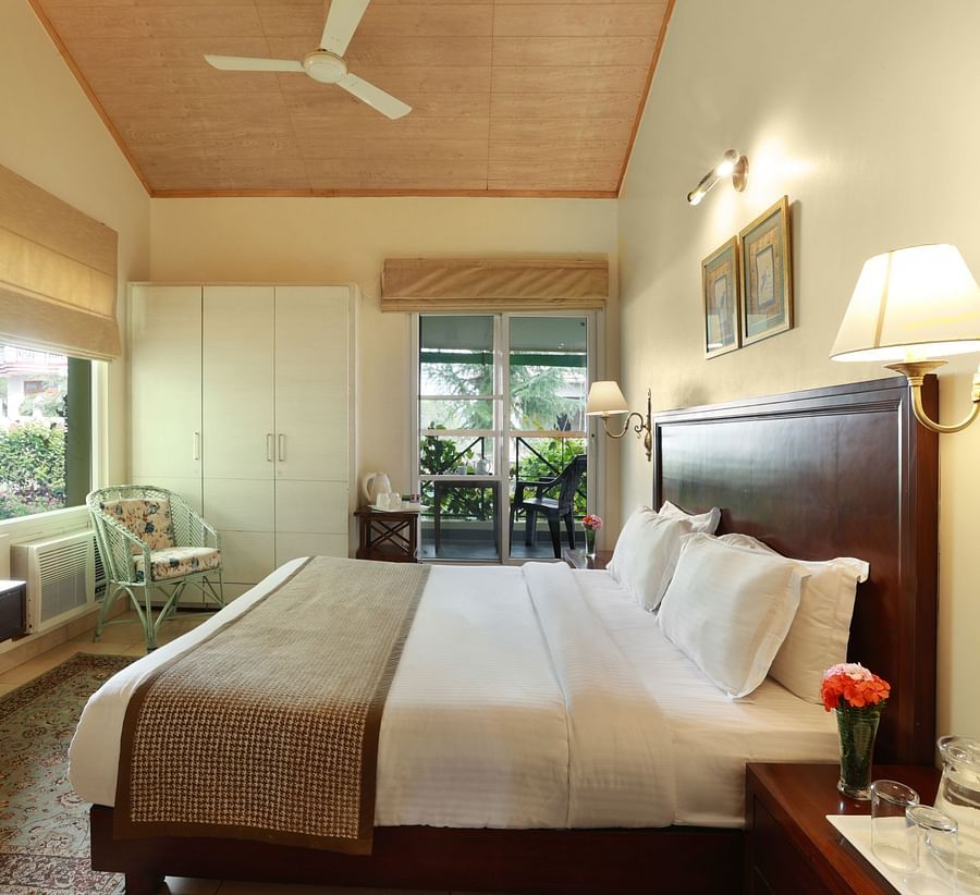 A grand room with a cosy setting showcasing windows with serene view and amenities like bedside lamps, a television, a wardrobe, etc. - Lamrin Norwood Green, Palampur