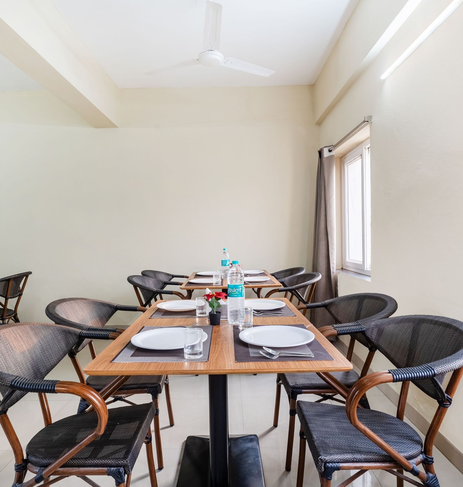 An empty dining area at Destino by Monday Hotels, Gachibowli, with 2 dining tables and woven chairs, set up with plates and water bottles.