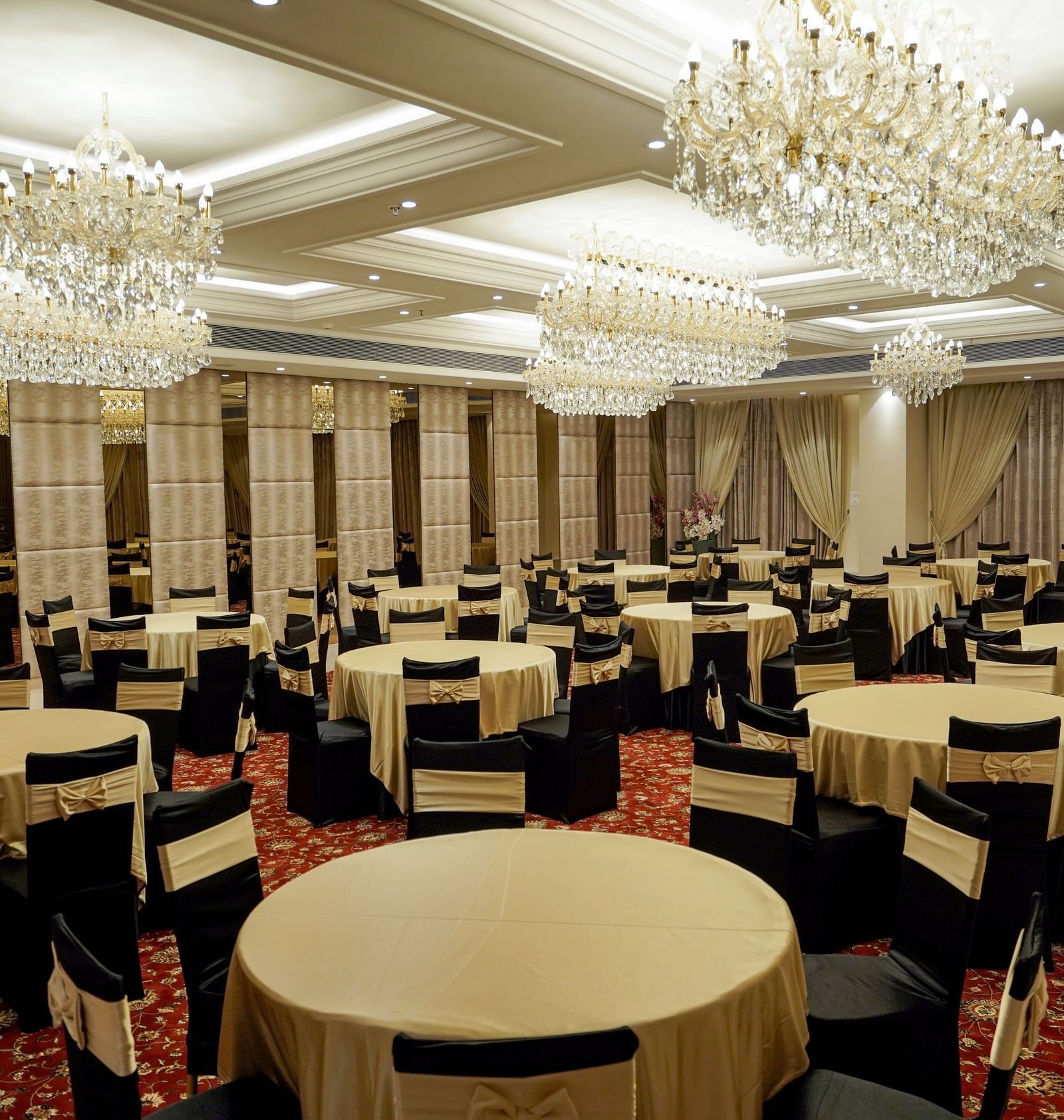 Corner view shot of the ballroom at M2 Square by Monday Premium featuring various tables surrounded by black coloured chairs.
