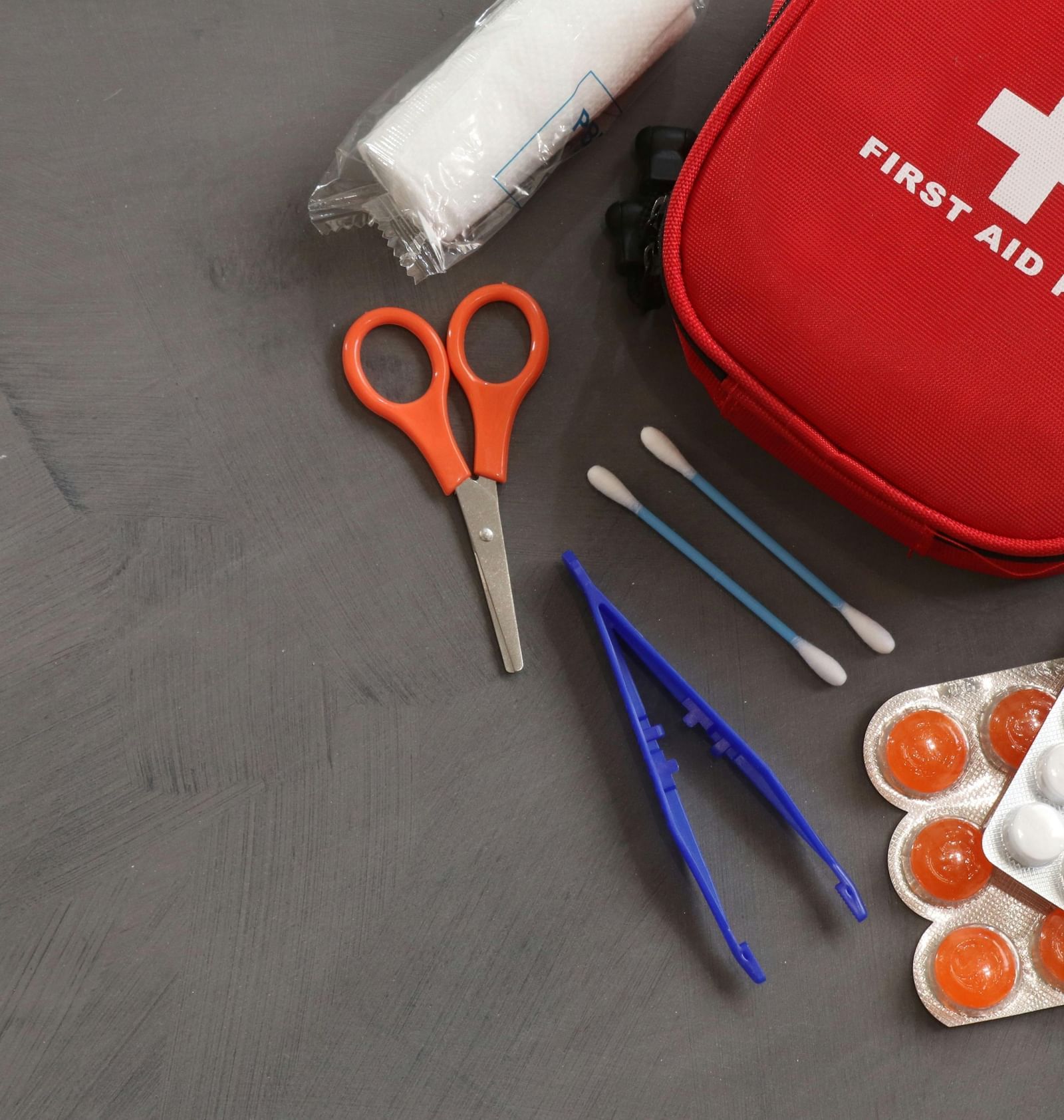 A red coloured pouch reading 'First Aid Kit' with several items and medicines scattered around it.