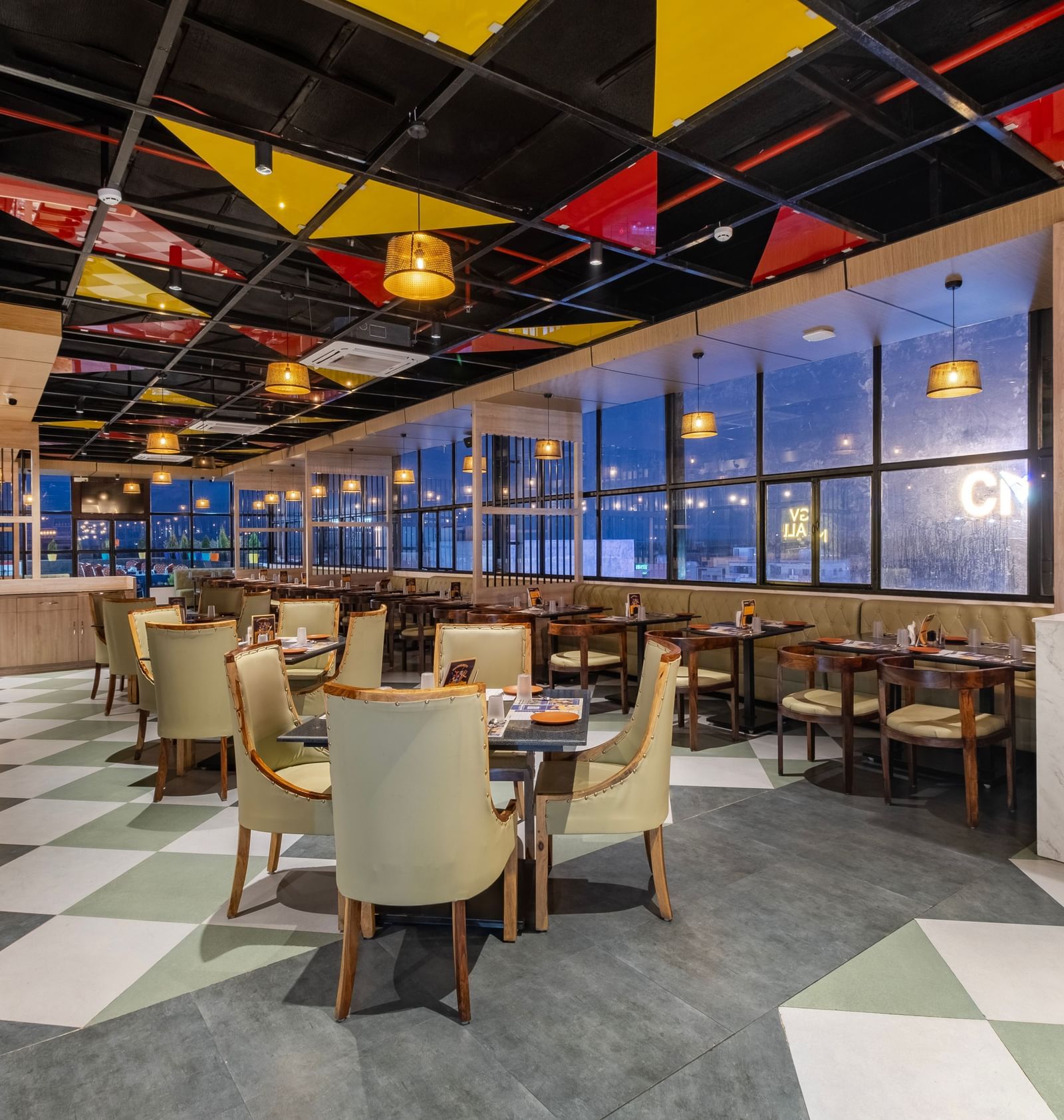 Restaurant at Monday Hotels Amalapuram Heights with colourful ceiling decor, city view, and neatly arranged tables and chair.