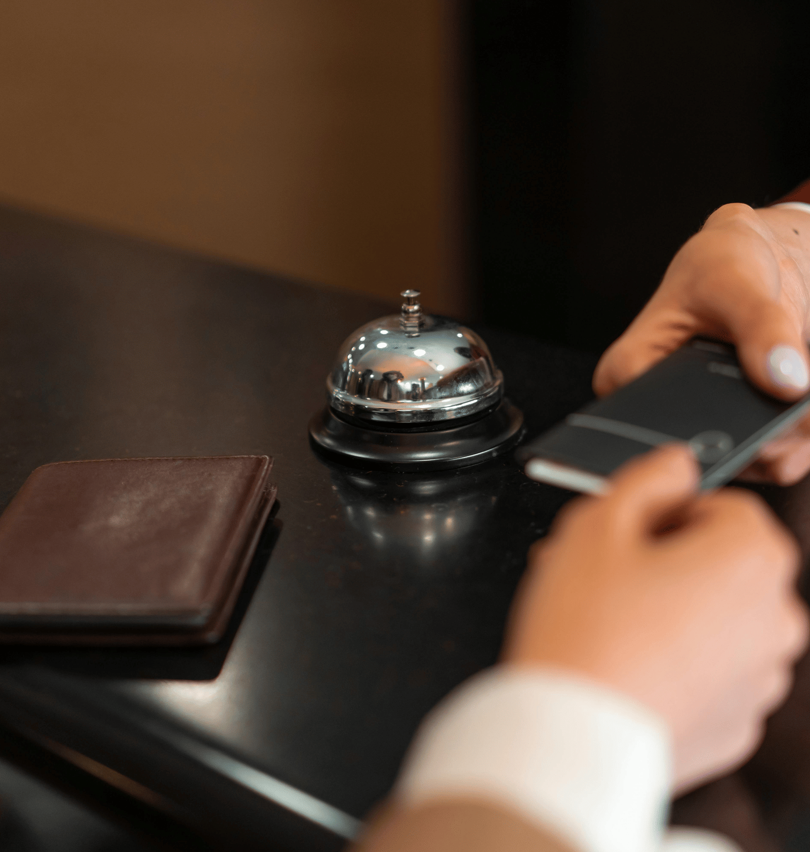 A hotel employee hands a black room key card to a customer across a dark reception desk with a bell.