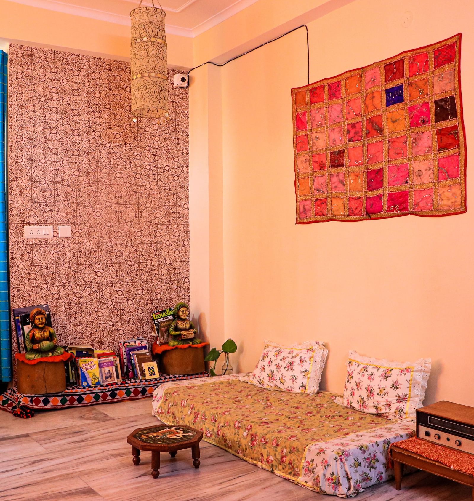 A room with a low bed, cushions, wall hanging, floor seating, and decorative elements on shelves at Jaypore360 Homestay in Jaipur.