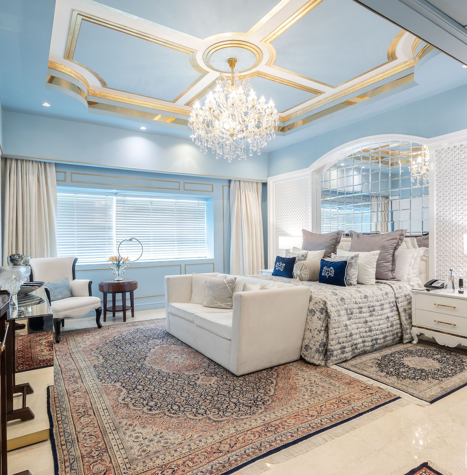 An image of a suite with a large bed and a sofa placed in front of a television and a chandelier hanging from the ceiling