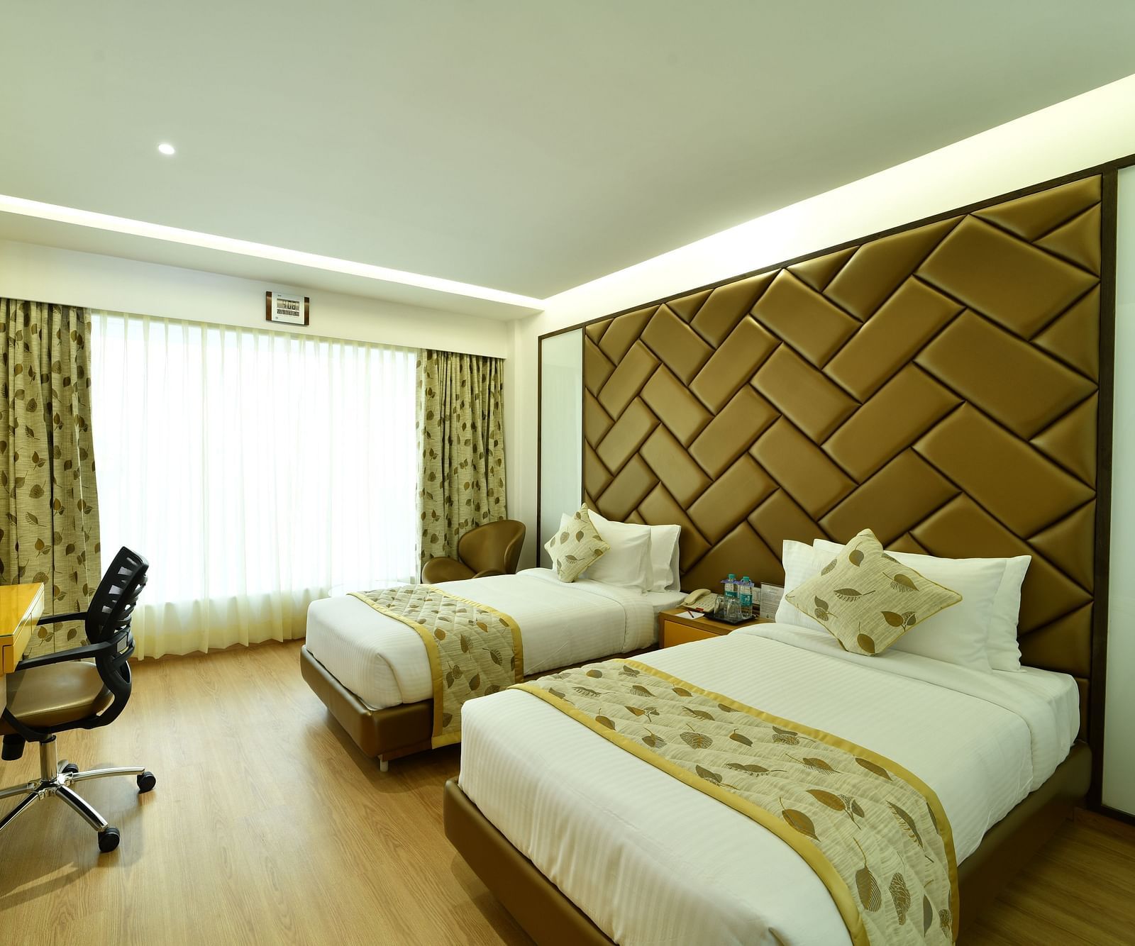 An image of hotel room with twin beds, warm lighting, and a large window with curtains -The President Hotel, Kumara Park, Bangalore