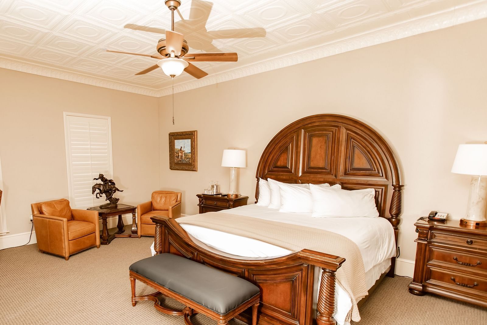 Bedroom with wooden bed and leather seating at The Grand Hotel & Ballroom, McKinney.