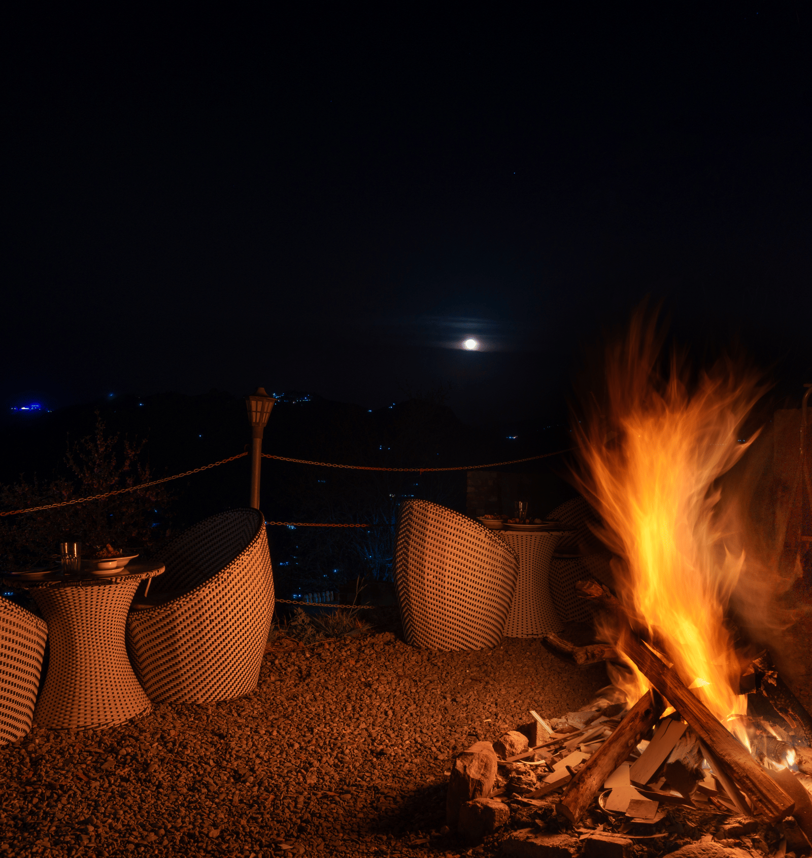 A glowing bonfire at night surrounded by comfortable outdoor chairs under a dark sky at Himalayas Resort By The Lake Hill, Mukteshwar.