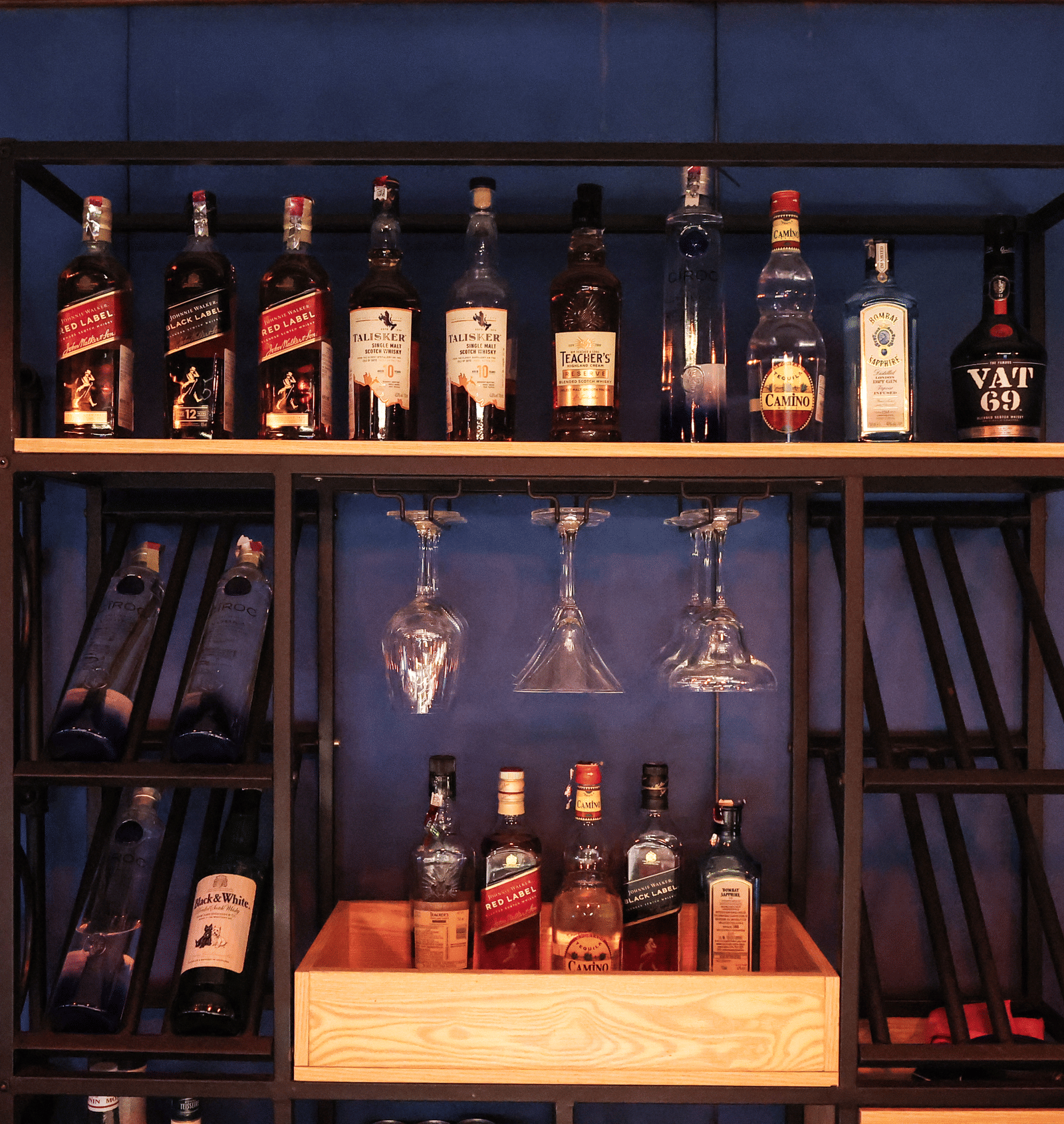 Close-up of the industrial-style black metal bar shelving with bottles of wine, spirits, and hanging glassware at Hotel Hukam's Lalit Mahal.
