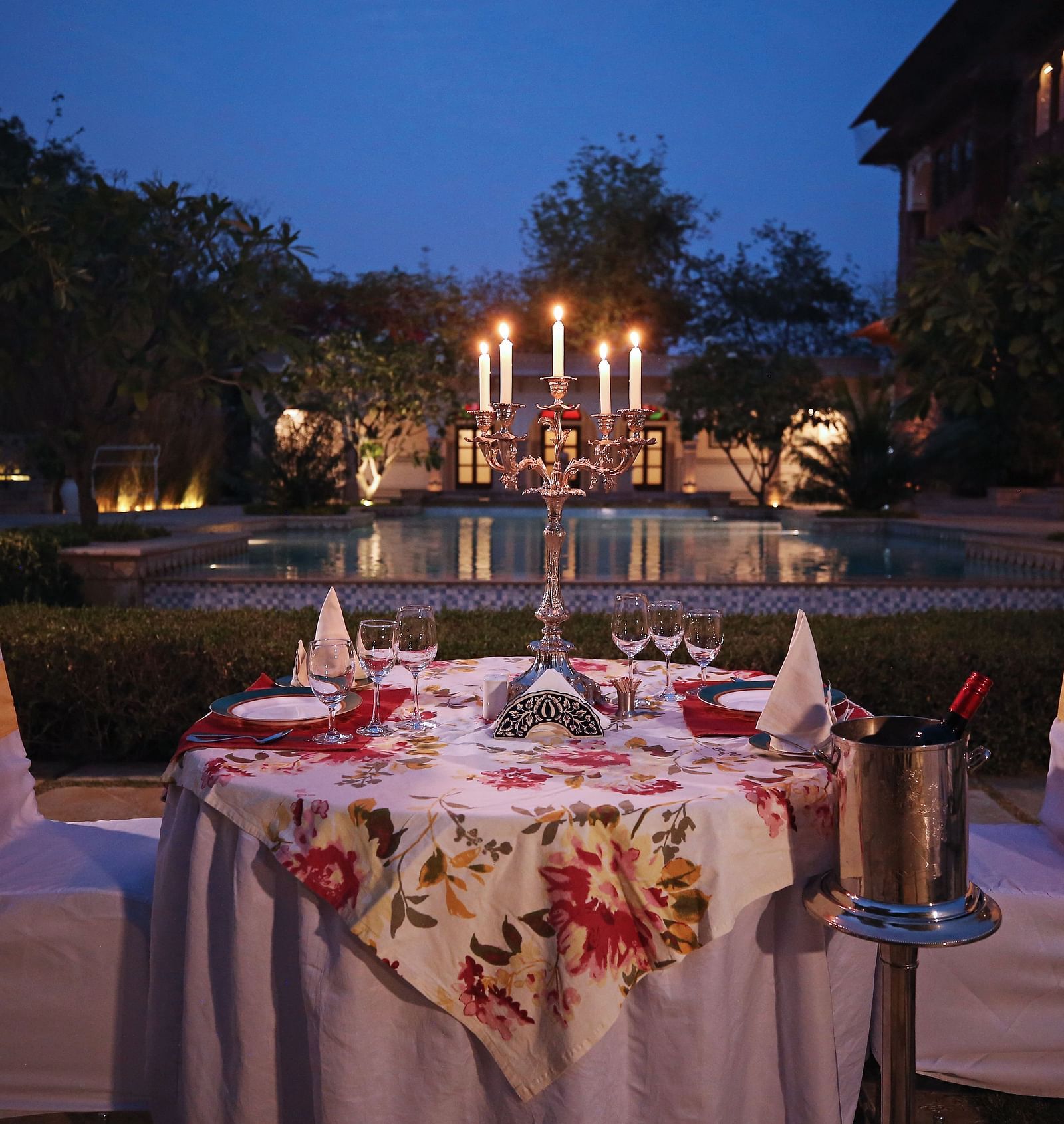  A table set for a romantic dinner by a swimming pool at dusk, illuminated by candles - Khas Bagh, Jaipur.